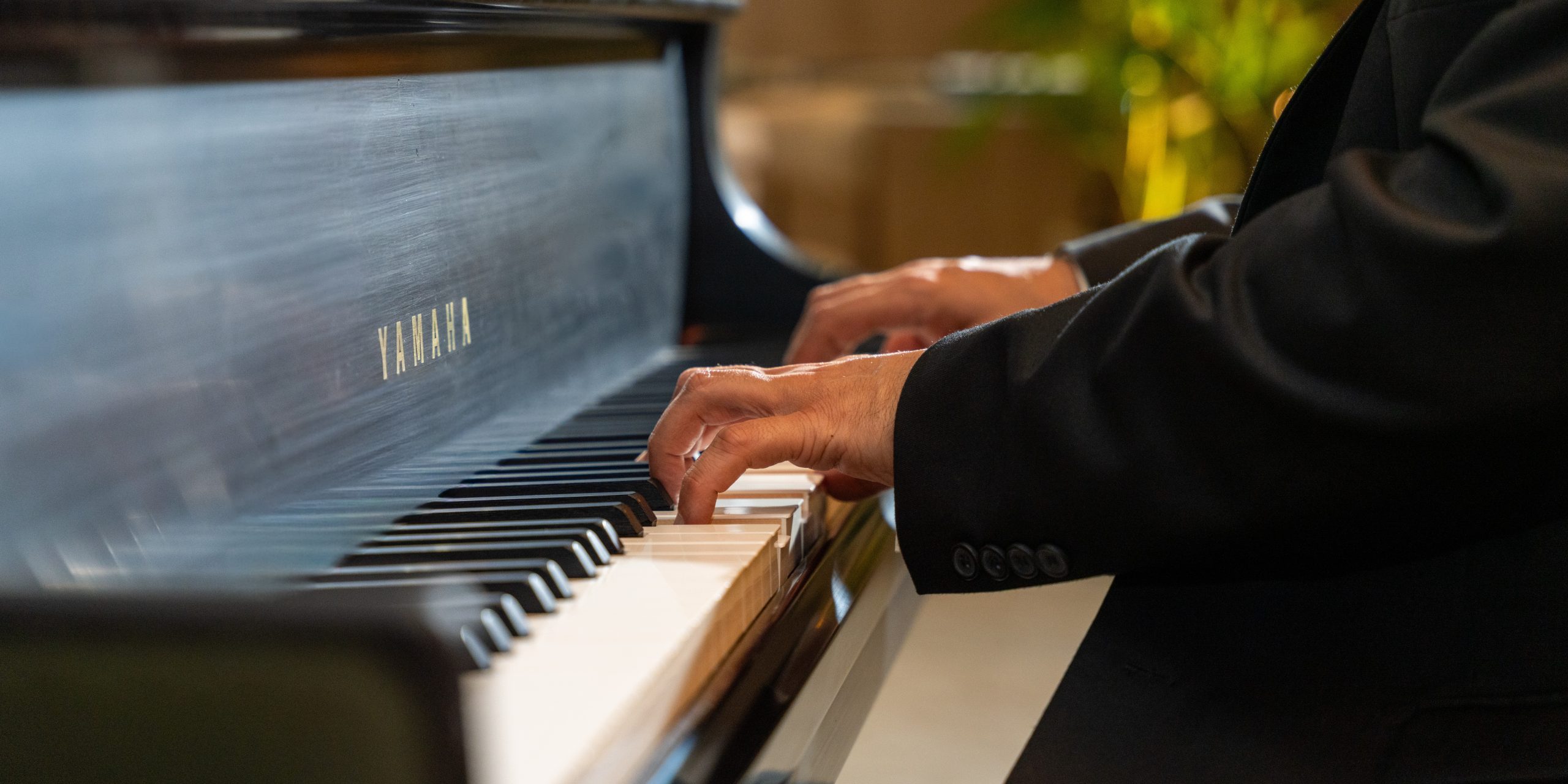 Close‑up of hands playing a Yamaha piano, with the brand name visible on the glossy black surface.