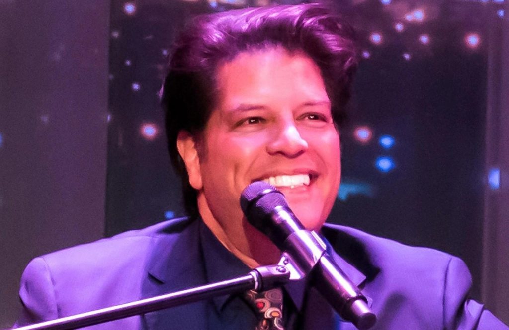 George bugatti singing onstage with a warm smile.