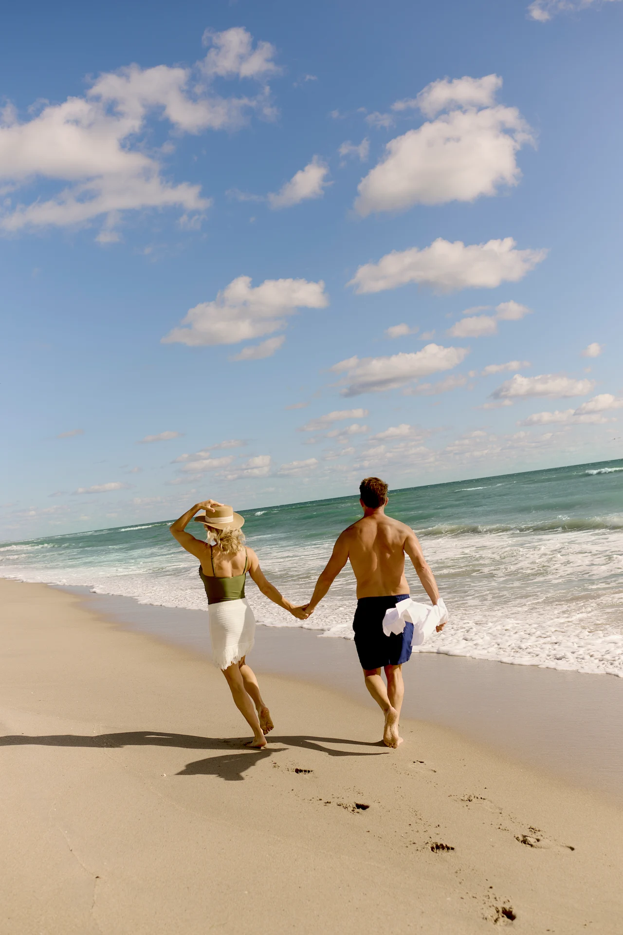 Couple walking hand in hand along a sandy beach with gentle waves and soft afternoon light.