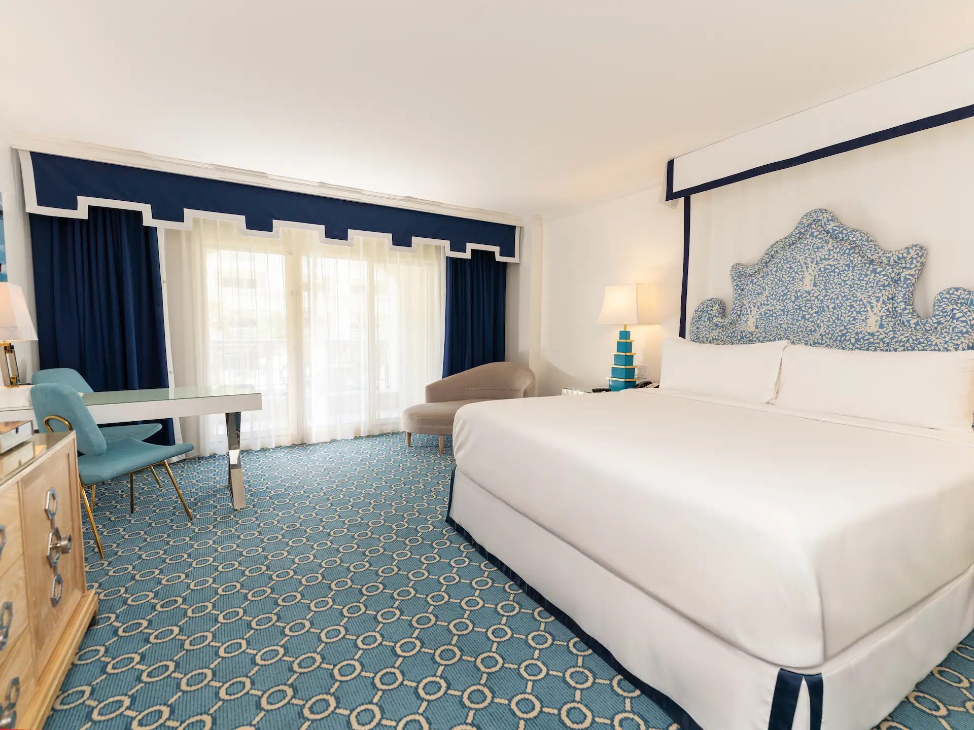 Bright coastal-inspired hotel room with blue accents, patterned carpet, and a large bed with a coral-style headboard.
