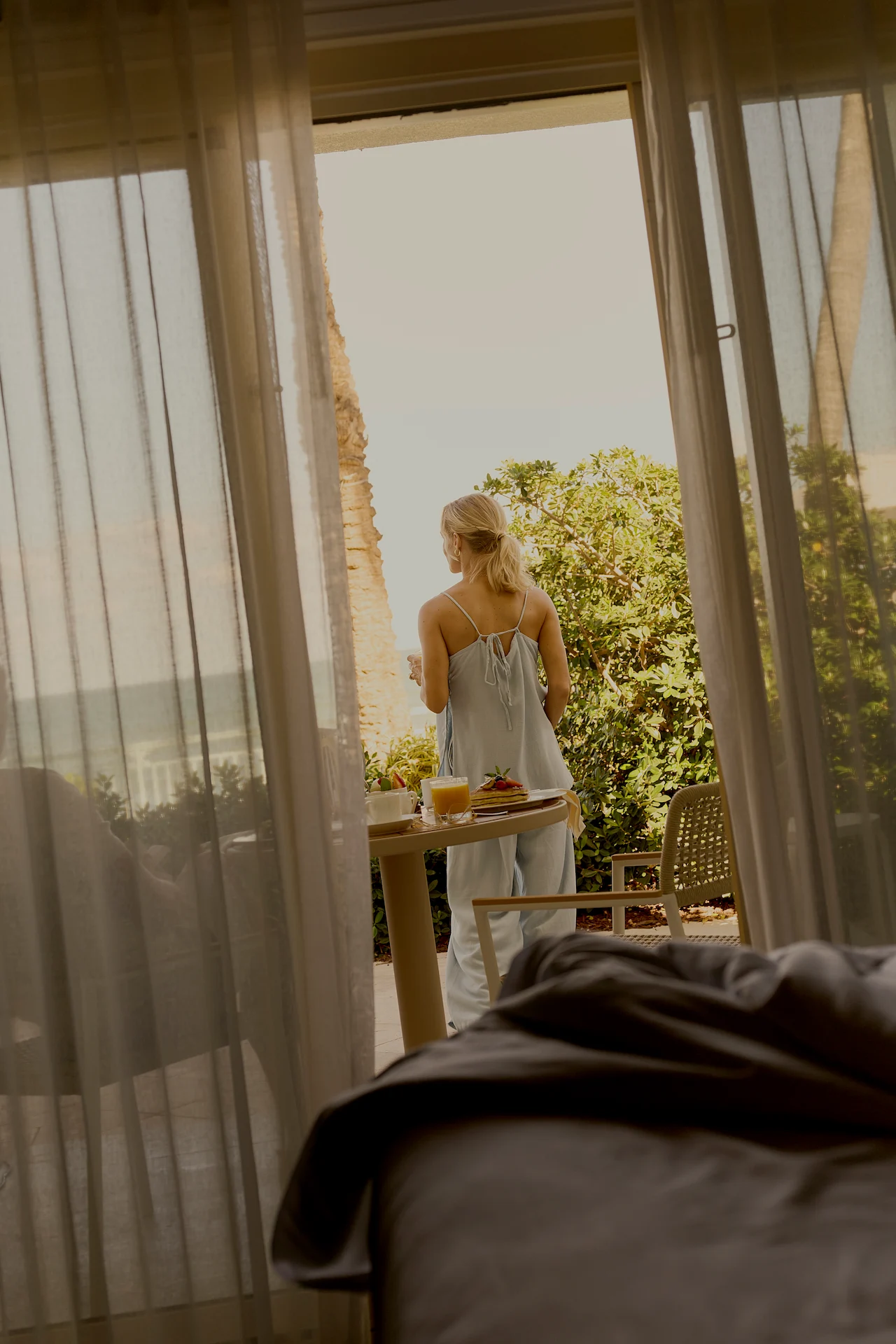 Guest enjoying in-room breakfast on a terrace overlooking lush tropical gardens.