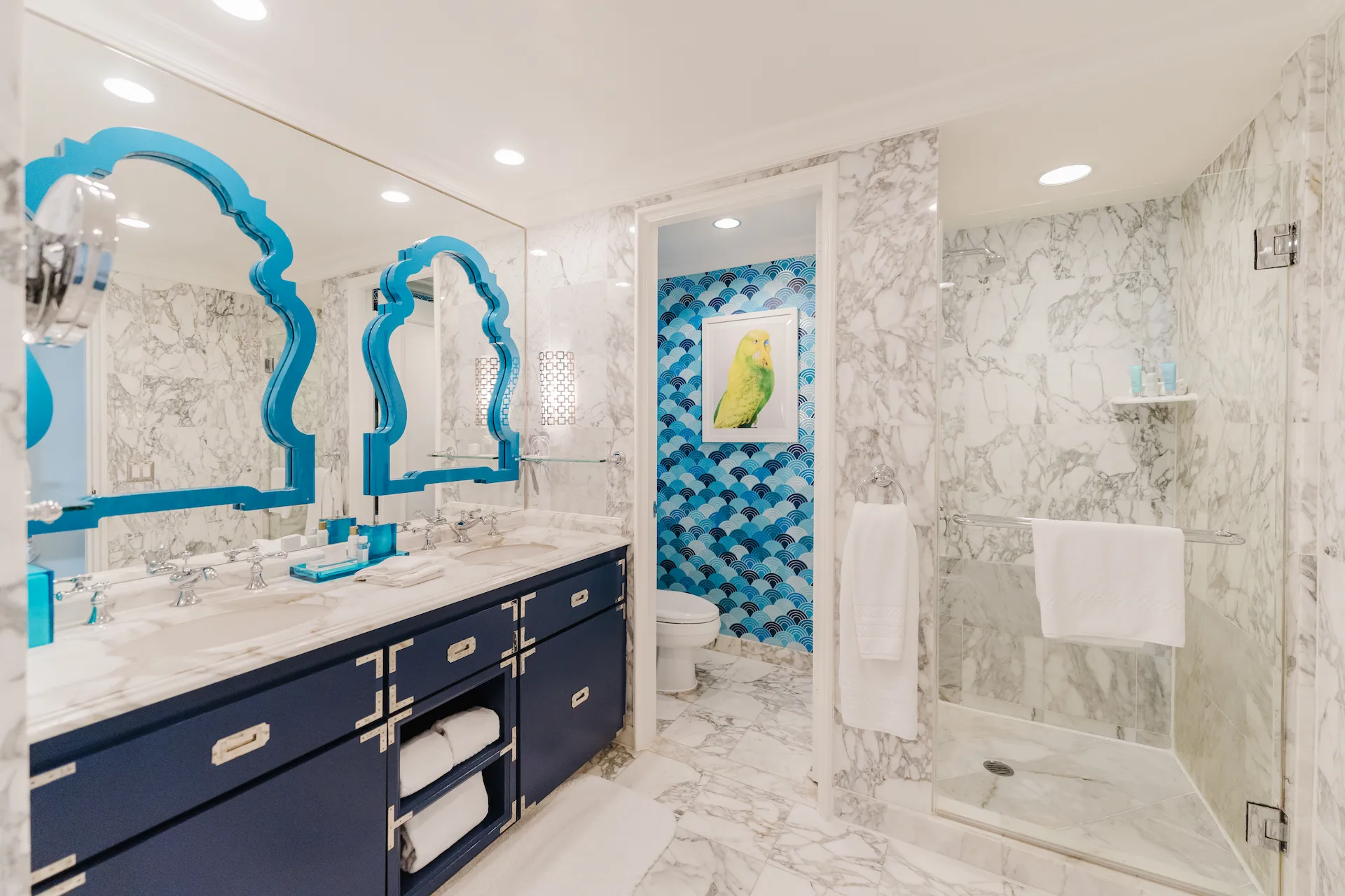 Luxurious bathroom with double vanity, blue-framed mirrors, marble surfaces, and a glass-enclosed shower.