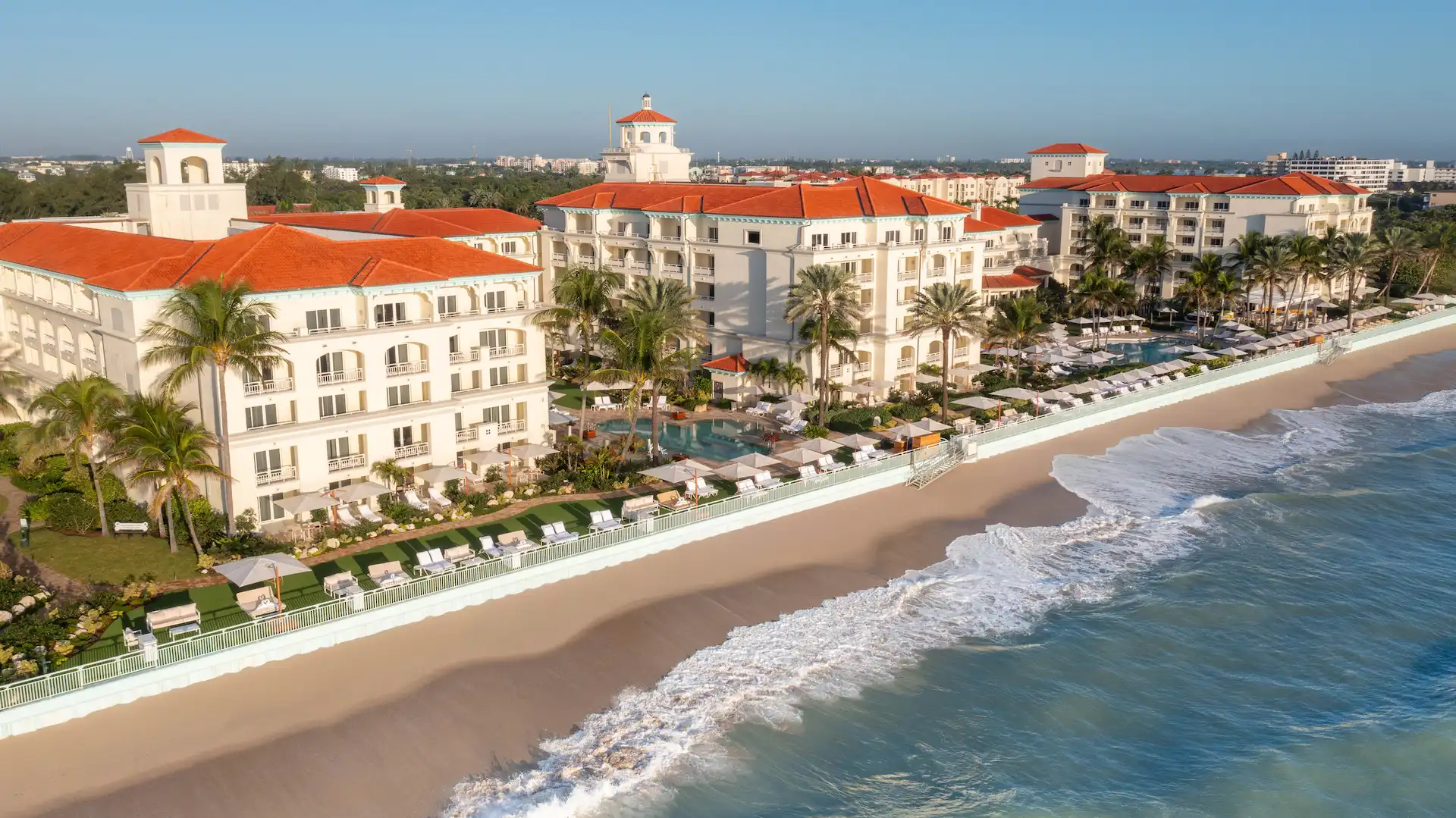 Aerial view of eau palm beach resort with white buildings, red‑tiled roofs, pools, palm trees, and a sandy shoreline.