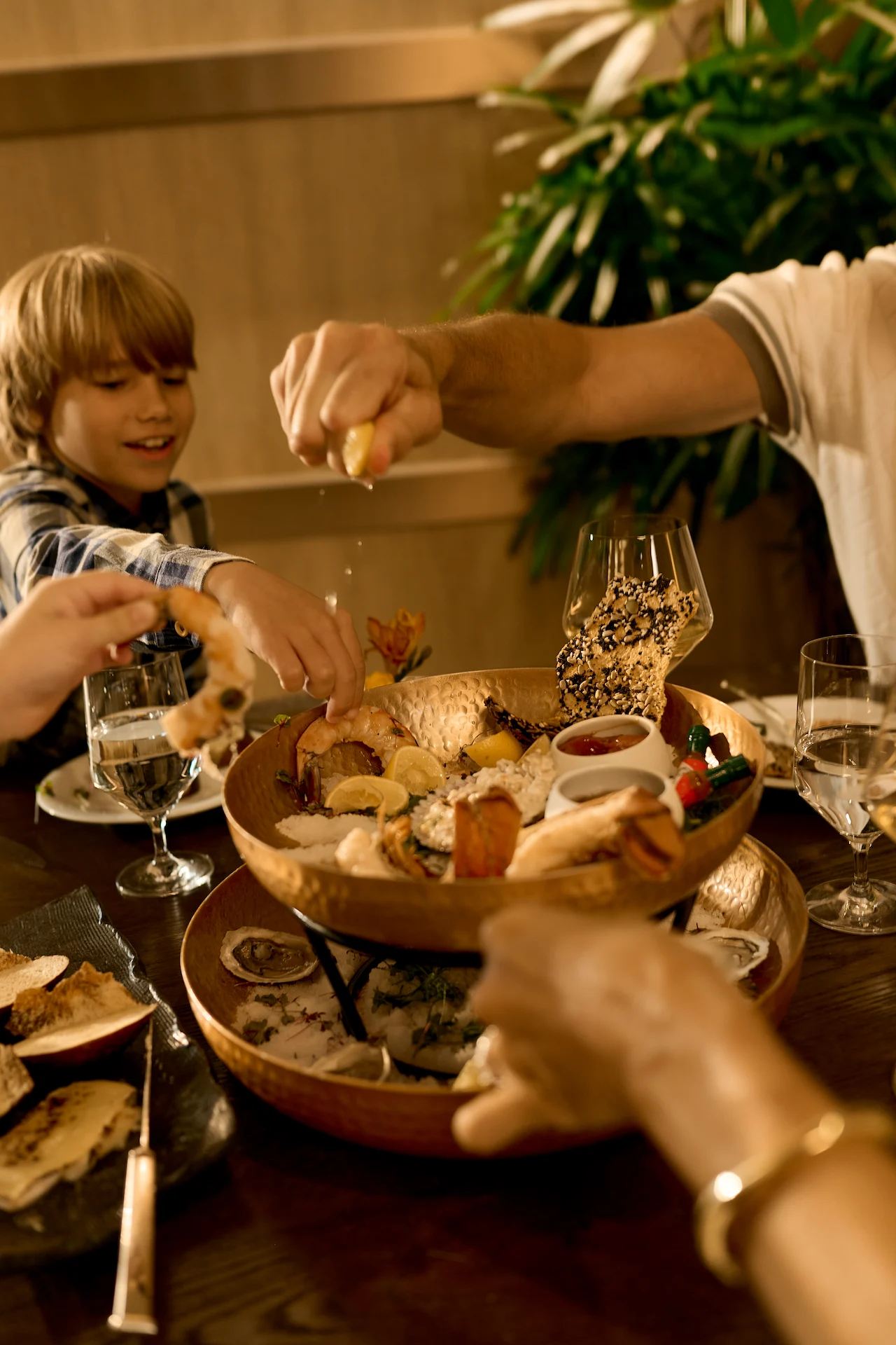 Hands sharing a seafood platter with shrimp, oysters, lemons, and sauces.