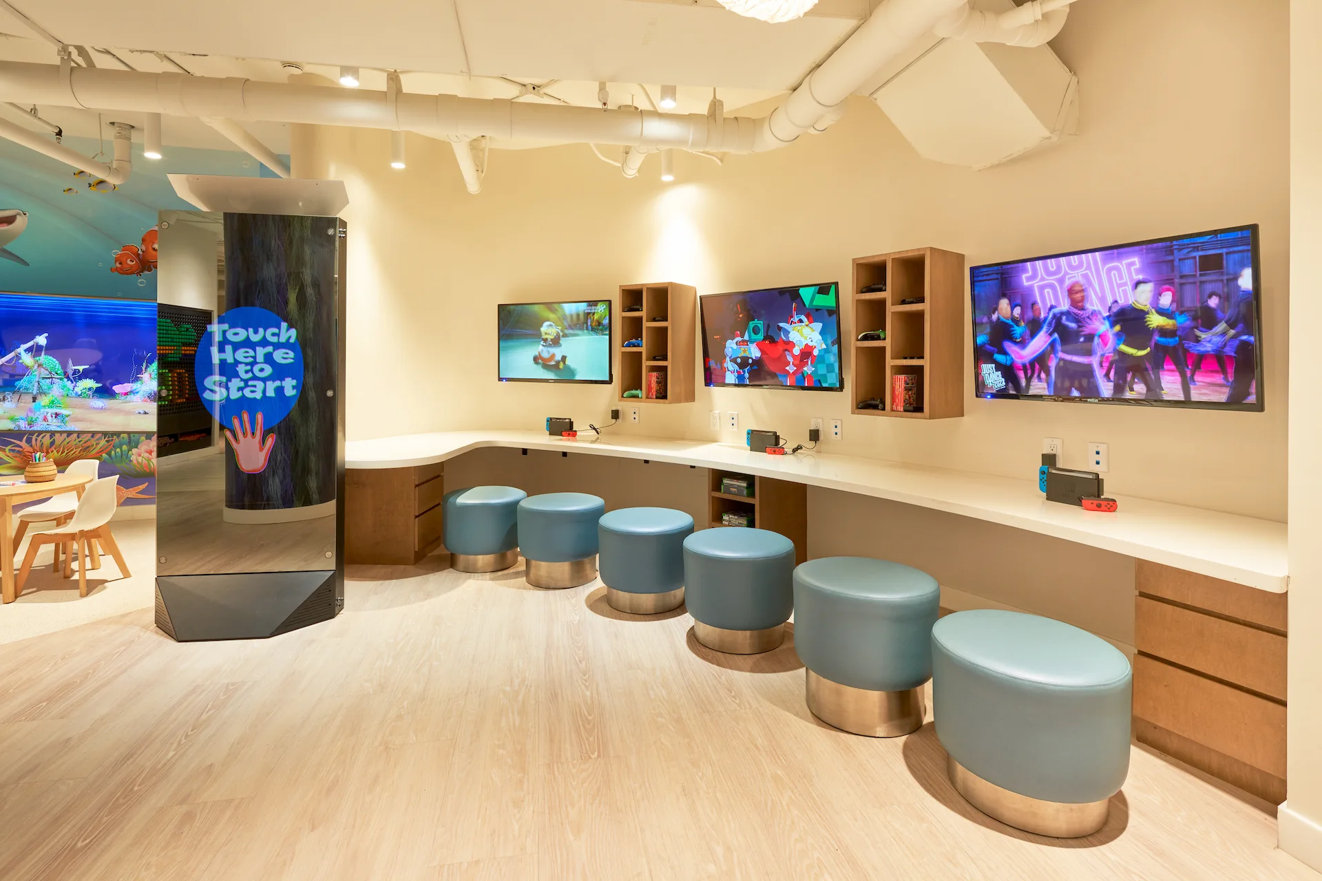 Kids’ gaming area with nintendo consoles, stools, and colorful screens.