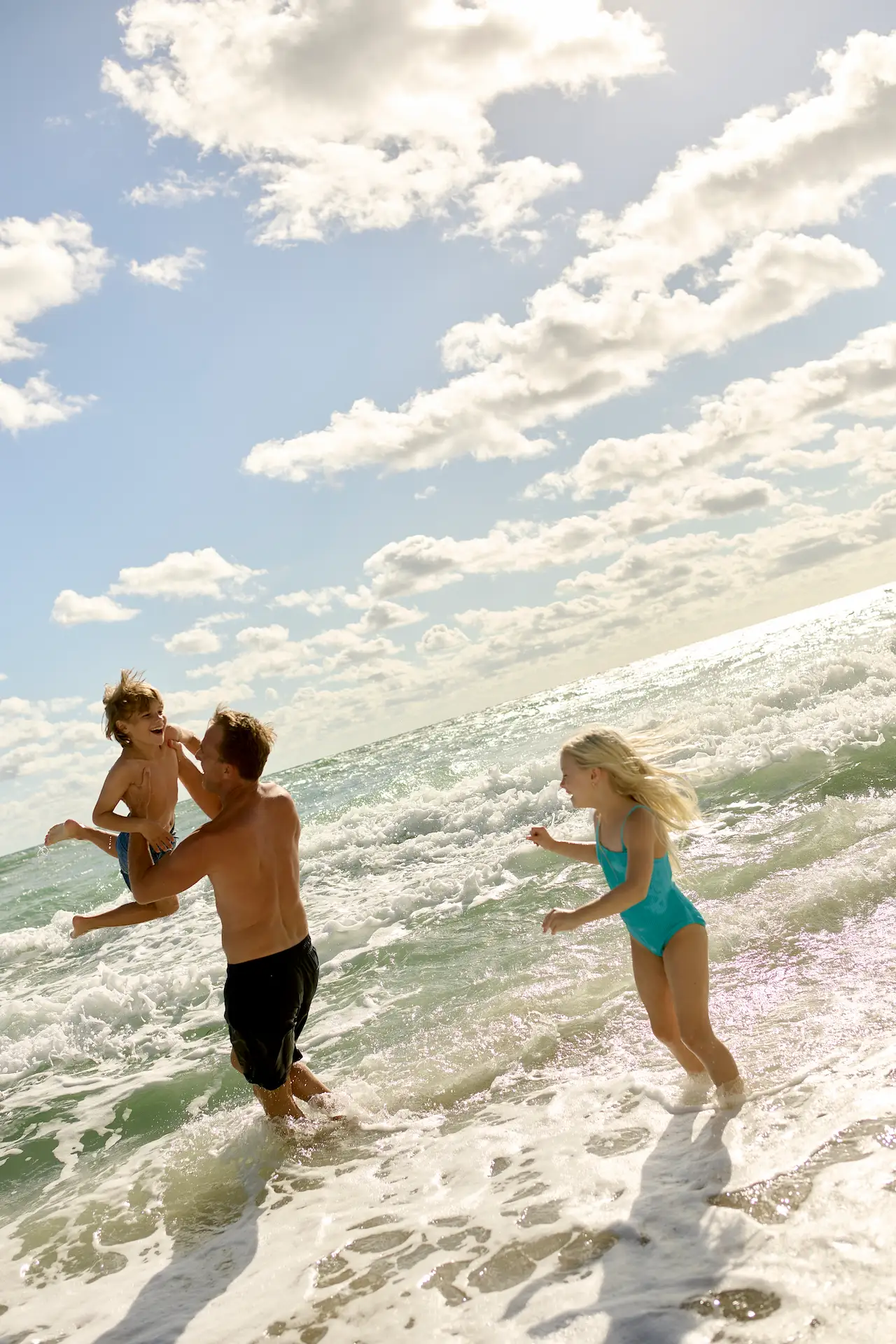 A family enjoying a sunny beach day, playing together in the ocean waves.