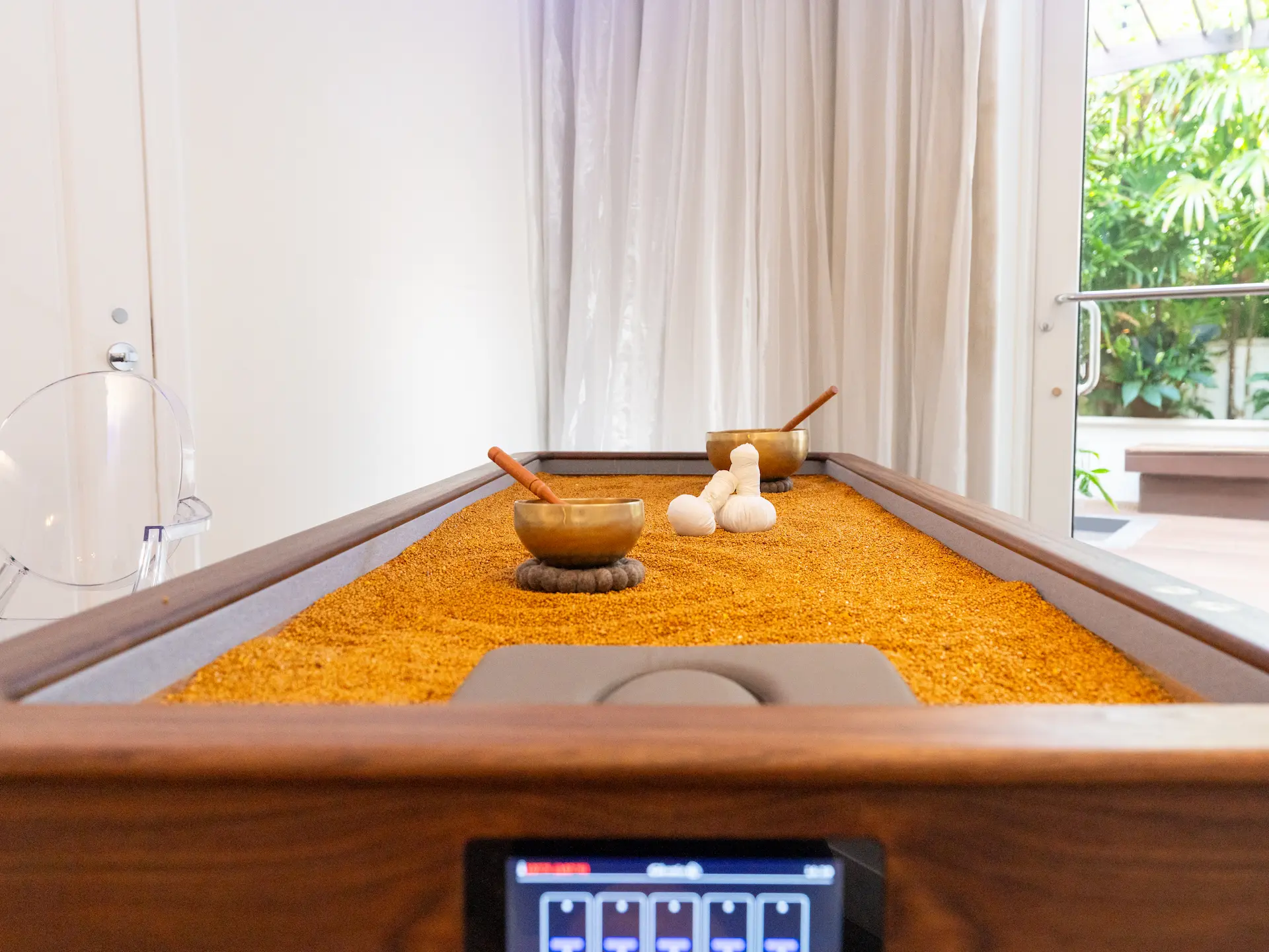 A wellness table prepared with warm sand, herbal compresses, and sound‑therapy bowls in a calm spa setting.