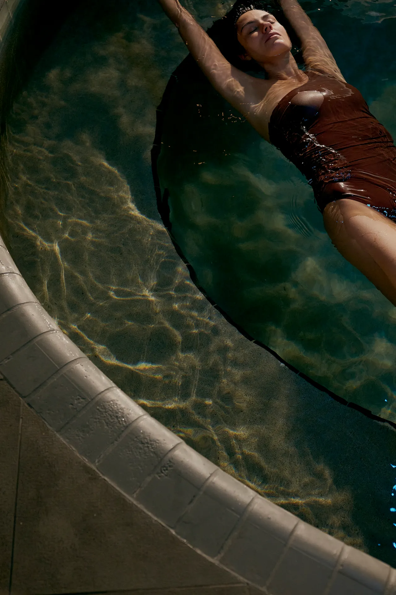 A person floating calmly on their back in a circular pool, with sunlight reflecting across the water.