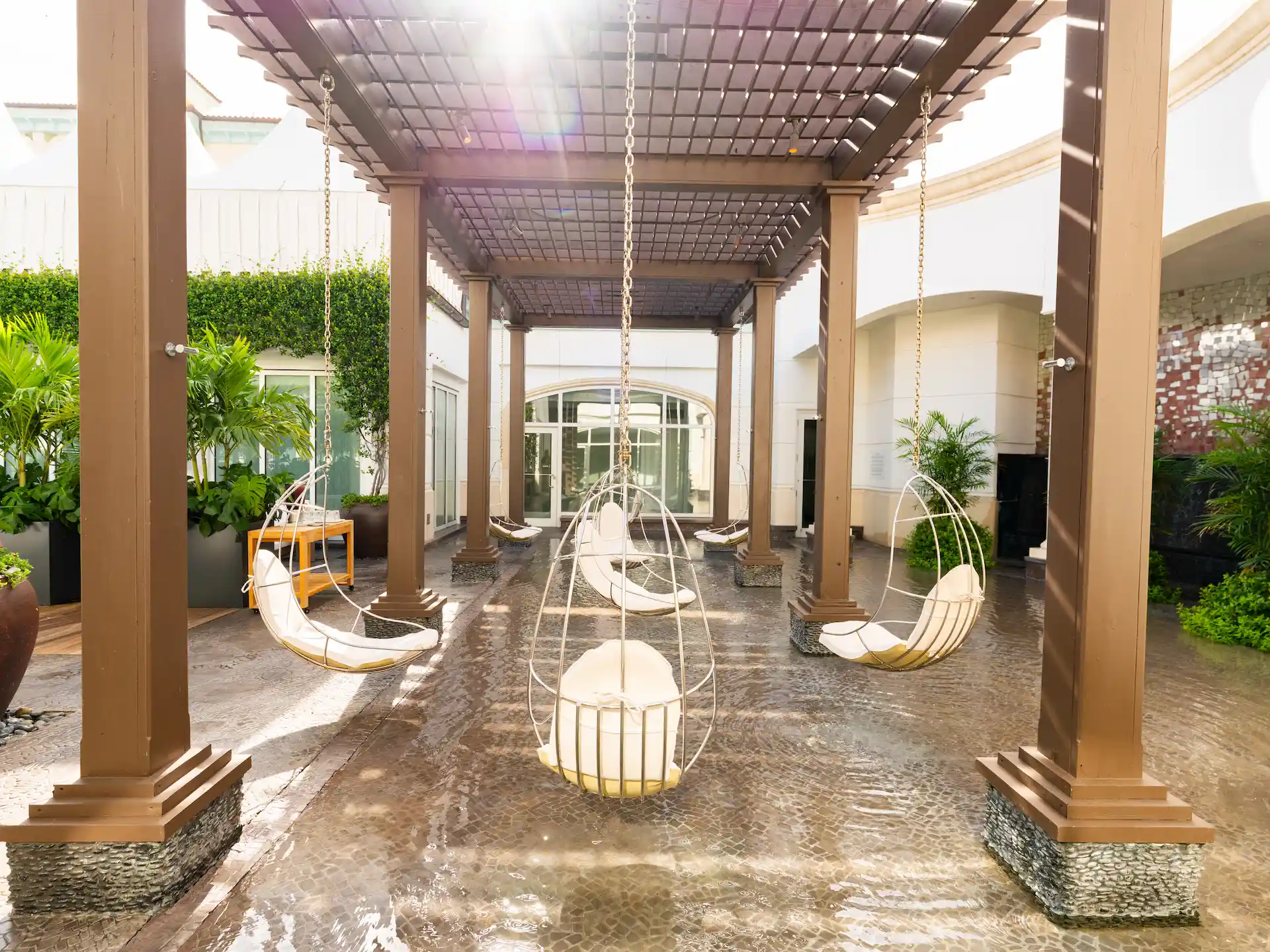 Hanging chairs under a wooden pergola, surrounded by greenery and soft sunlight.