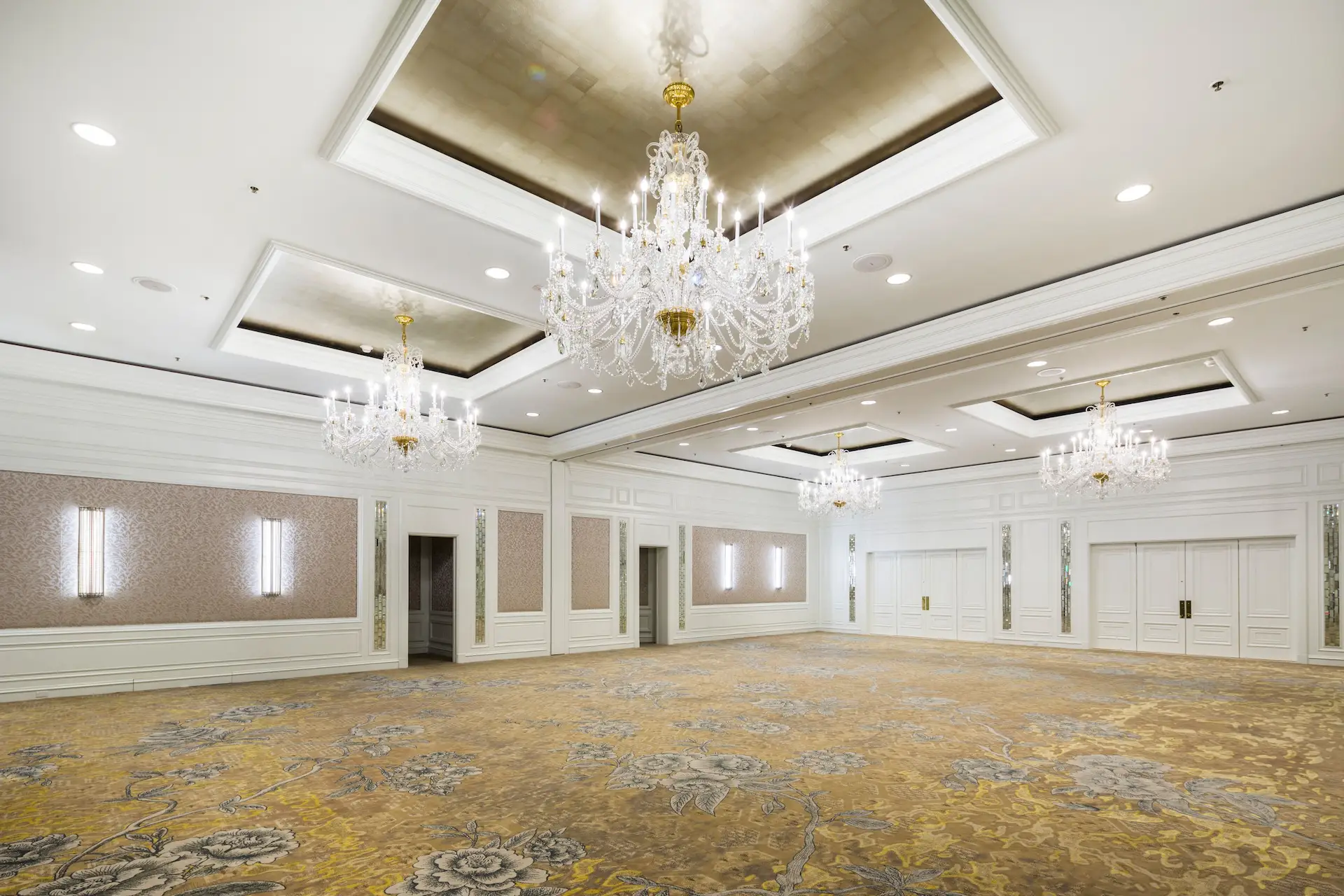 A grand ballroom with crystal chandeliers, decorative paneling, and a spacious layout ready for formal events.