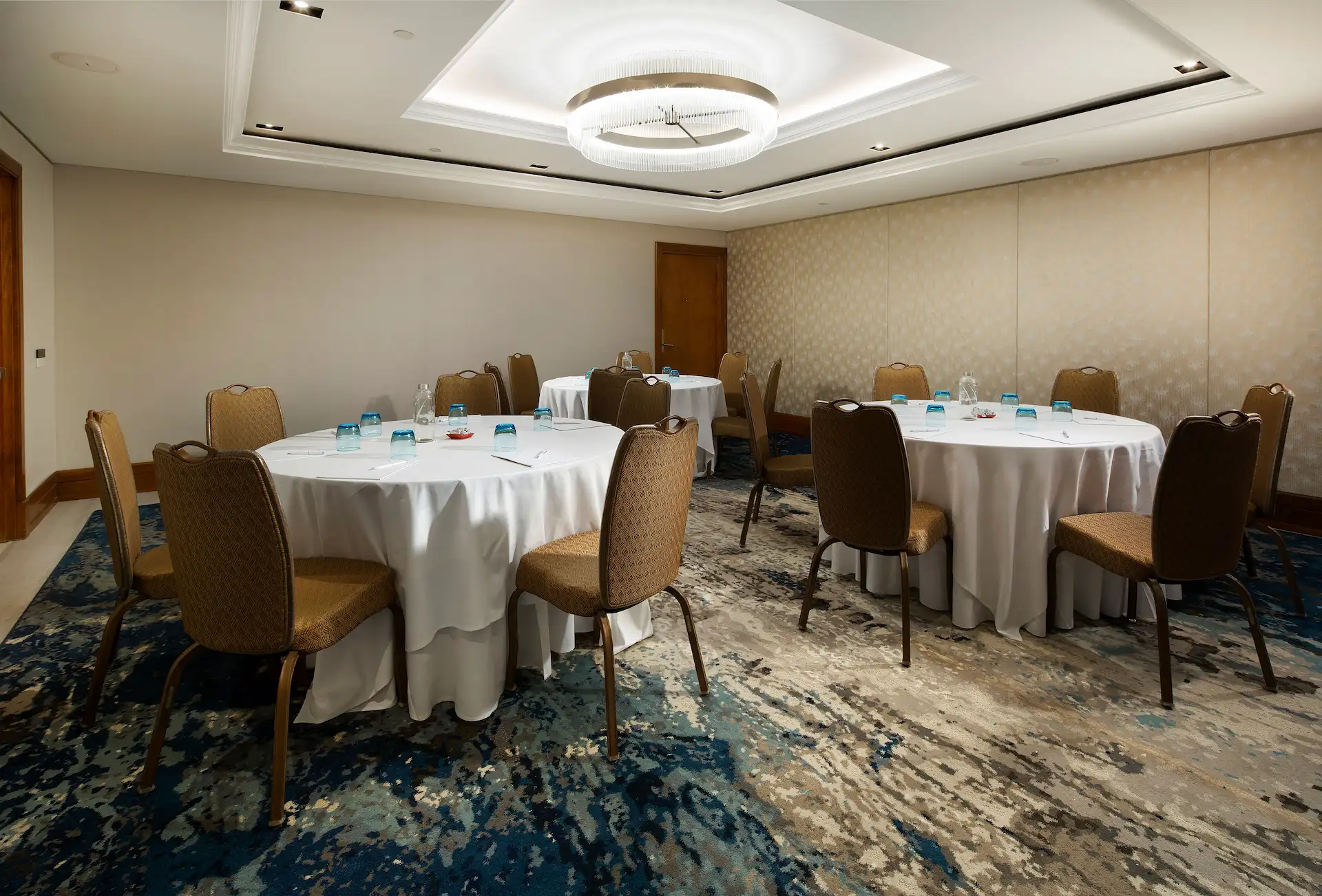 A meeting room with round tables set with water glasses, notepads, and chairs arranged for a conference.