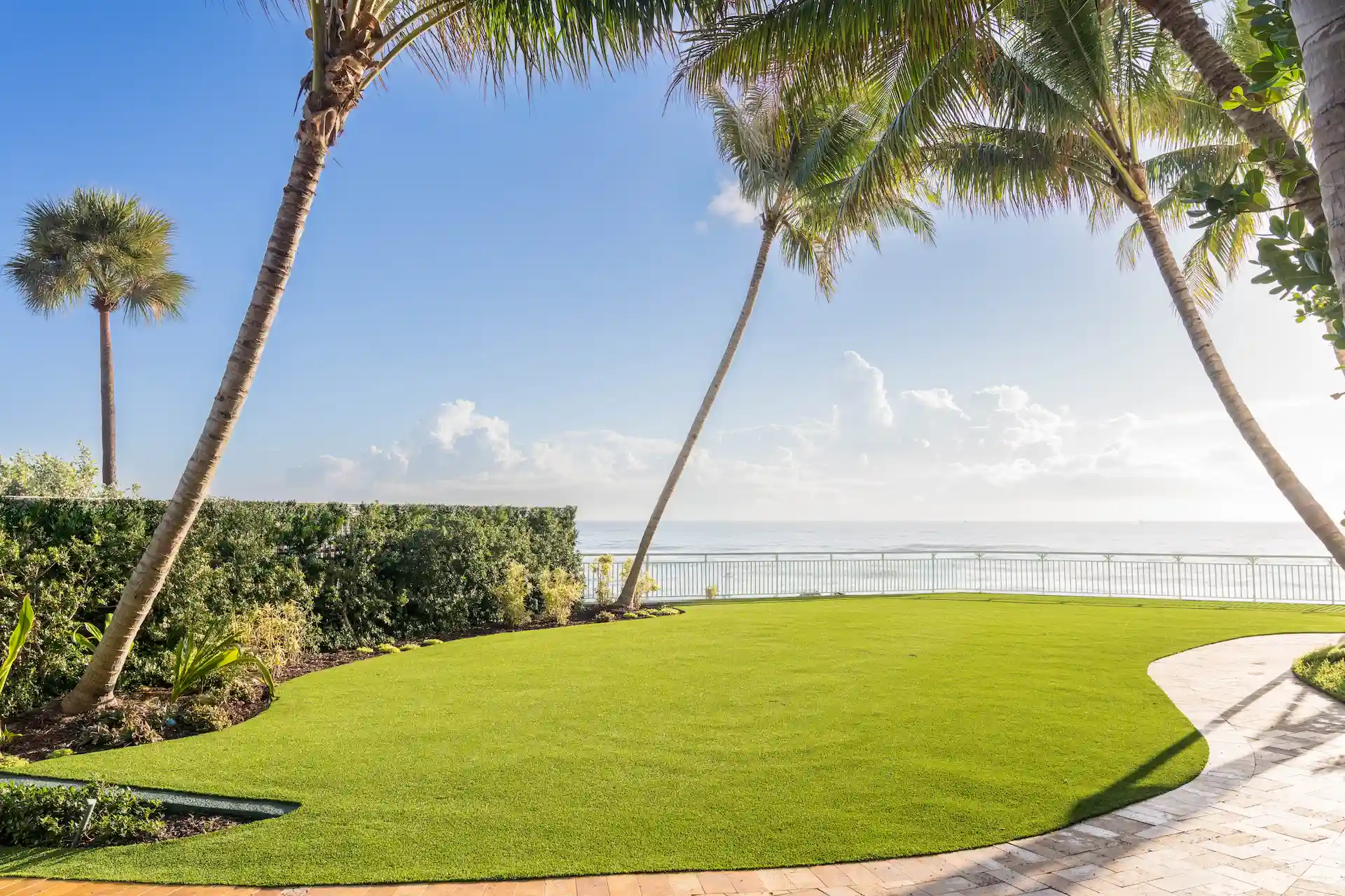 Lawn and palm trees overlooking the ocean, framed by a curved pathway and tropical landscaping.