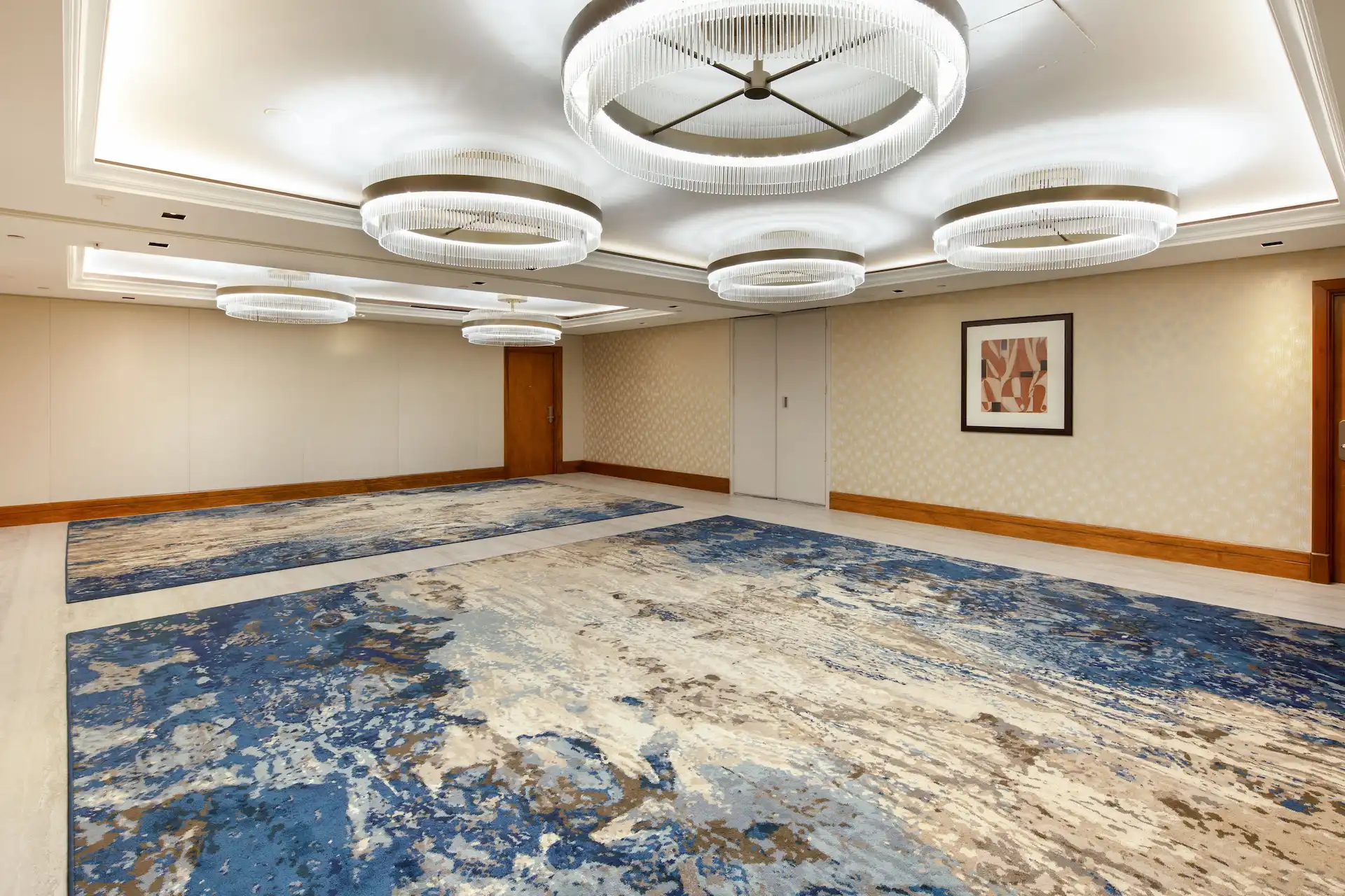Spacious event room with crystal chandeliers, patterned carpet, and light-colored walls.