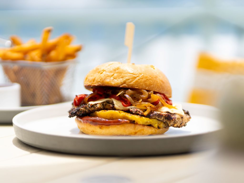 Gourmet chicken sandwich with melted cheese and peppers on a toasted bun, served with fries in the background.